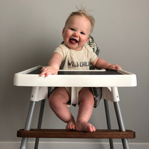Baby wearing Wild Child onesie, in IKEA high chair.